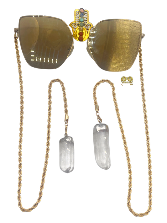 Step into your own celestial realm with "Aligned" glasses by Orion Elise. Gold and brown frame with durable gold chain adorned with clear quartz crystals. Intricate Hamsa hand motif at center of frames representing all seven chakras.