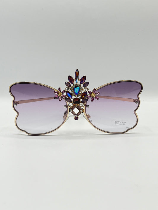 "Carnival Wings" fashion eyewear by Orion Elise, featuring a silver butterfly-shaped frame with purple and pink gradient lenses and a diamond-encrusted charm at the center. A celebration of freedom, joy, and festivity, perfect for music festivals, carnivals, or adding whimsy to any outfit.